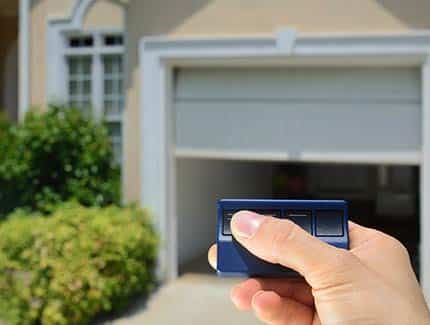 a hand using a garage door opener remote in front of a home garage