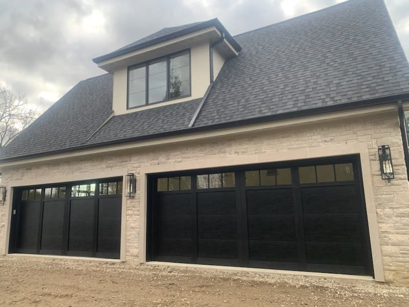 Light-colored garage door on a stone-front home with a covered front entry