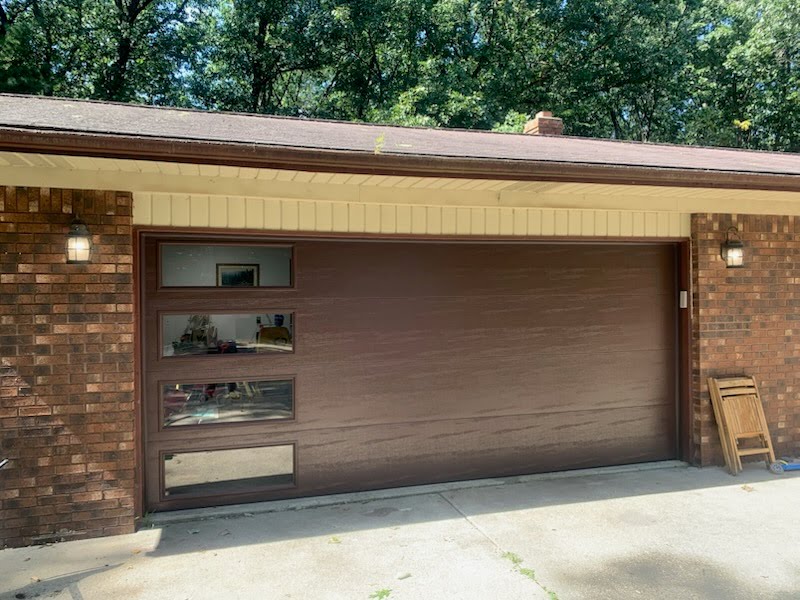 White detached garage with two carriage-style garage doors, dark shingled roof, and paved driveway beside a white house.